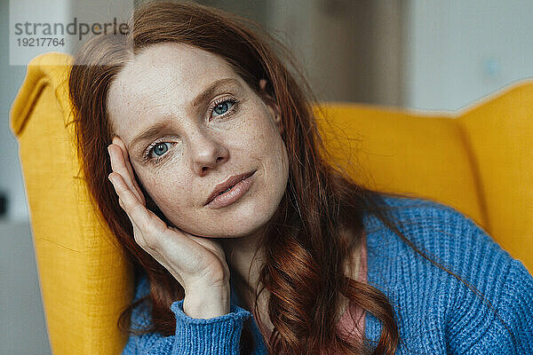 Redhead woman sitting on armchair at home