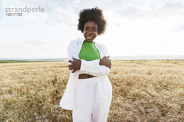 Happy young woman with curly hair hugging self in field