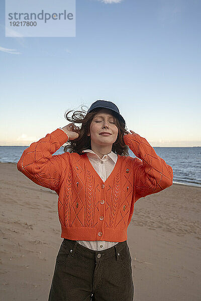 Junge Frau mit Hut steht am Strand