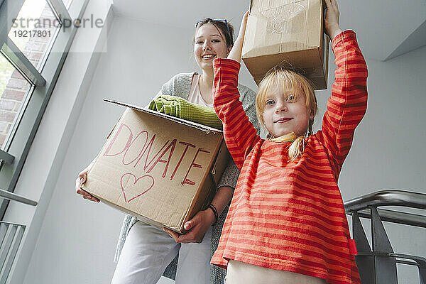 Girl carrying box on head by elder sister with clothes for donation