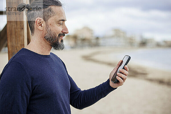 Reifer Mann benutzt Smartphone am Strand