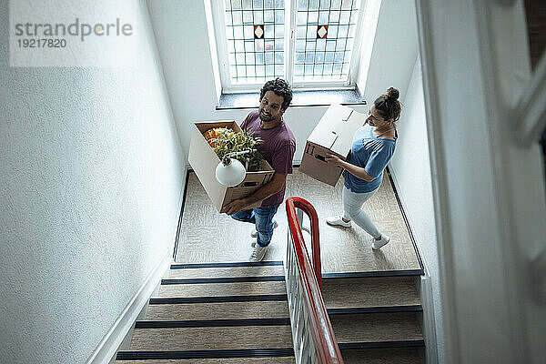 Lächelnder Mann und Frau mit Kartons  die die Treppe hinaufsteigen