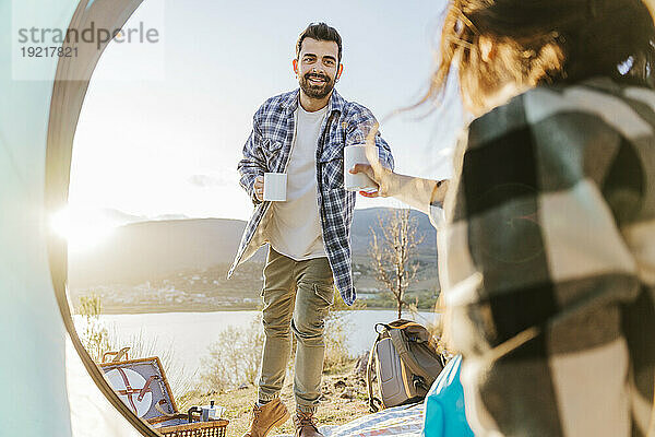 Smiling man giving coffee to woman inside tent