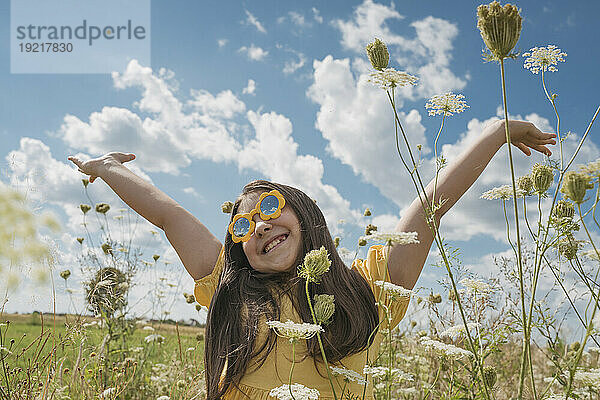 Fröhliches Mädchen mit erhobenen Händen genießt das Blumenfeld