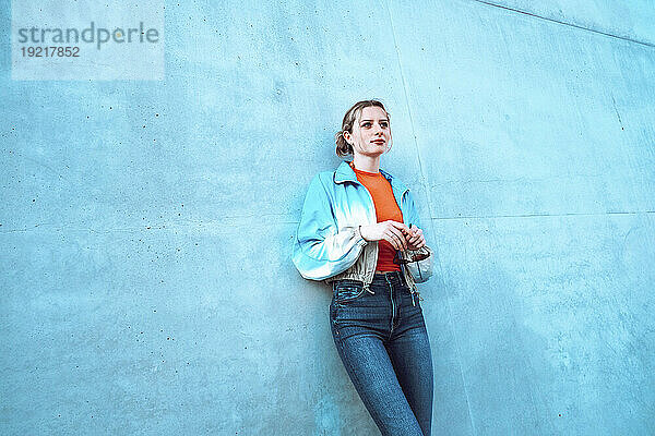 Frau mit Sonnenbrille lehnt an blauer Wand