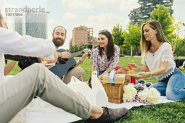 Lächelnder Mann spielt Gitarre mit Freunden und genießt Picknick im Park