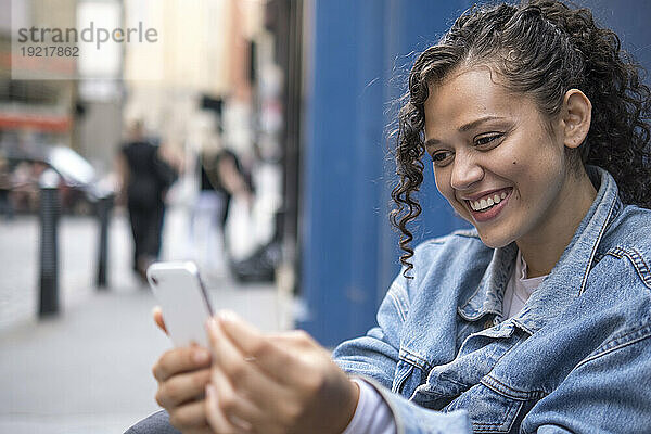 Glückliche junge Frau benutzt Smartphone am Fußweg