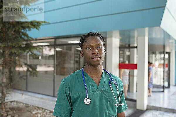 Junger Arzt mit Stethoskop steht vor dem Krankenhaus