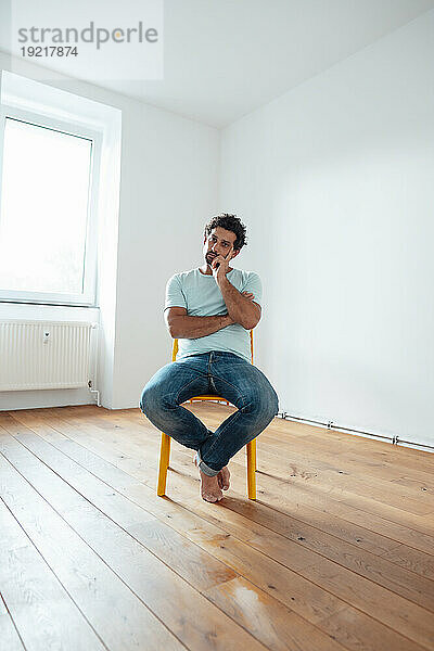 Nachdenklicher Mann sitzt zu Hause auf einem Stuhl vor der Wand