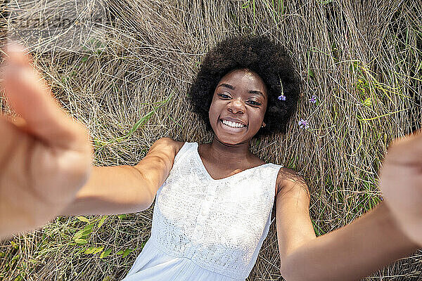 Glückliche junge Frau  die ein Selfie macht und sich auf trockenem Gras entspannt