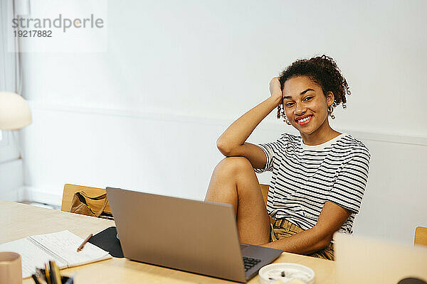 Smiling young student with laptop sitting at desk