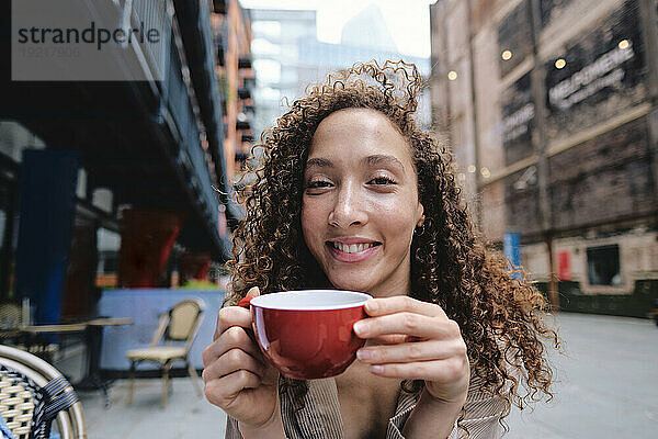 Glückliche Frau hält Kaffeetasse im Straßencafé