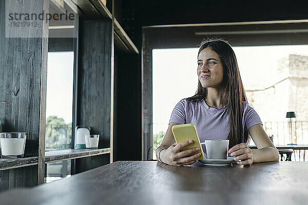 Portrait of pretty brunette sitting at office table with smart phone in hand