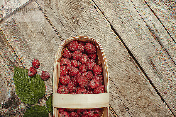 Wooden box with raspberries near leaf on table