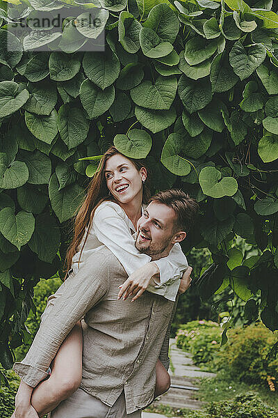 Smiling boyfriend giving piggyback ride to girlfriend in garden