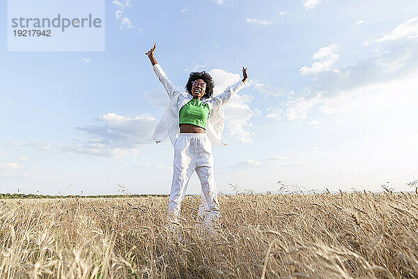 Carefree woman standing with arms raised in field