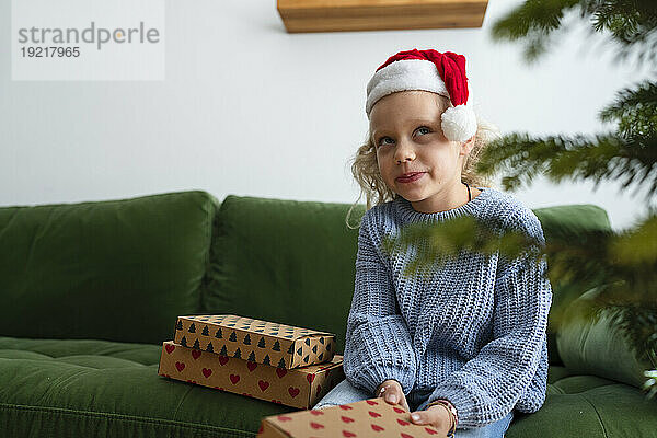 Nachdenkliches Mädchen sitzt mit Weihnachtsgeschenken zu Hause