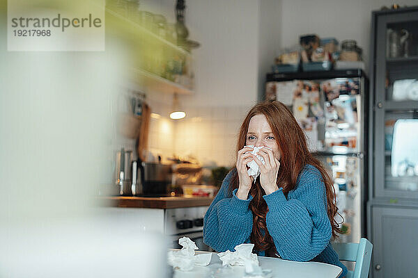 Kranke Frau putzt sich zu Hause die Nase auf Taschentuch