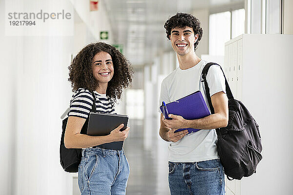 Lächelnde Studenten halten Aktenordner und Laptop im Flur
