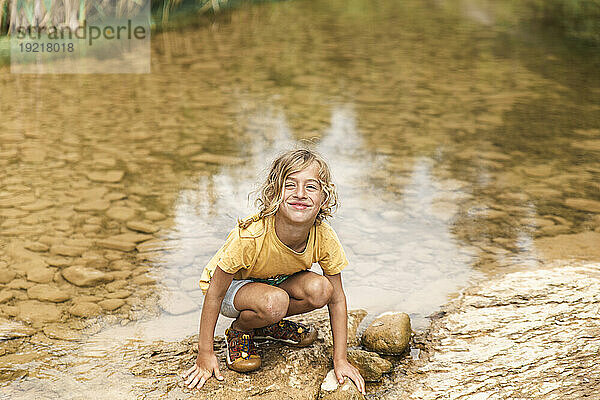Lächelnder Junge kauert am Fluss