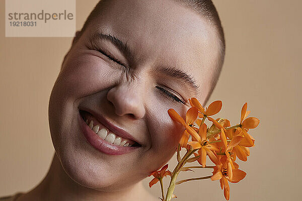 Glückliche Frau mit durch eine Blume geschlossenen Augen vor beigem Hintergrund