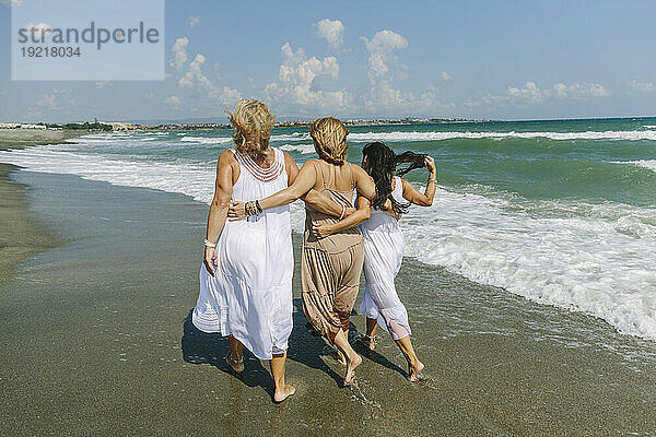 Frauen gehen mit den Armen umher und gehen gemeinsam am Strand in der Nähe des Meeres spazieren
