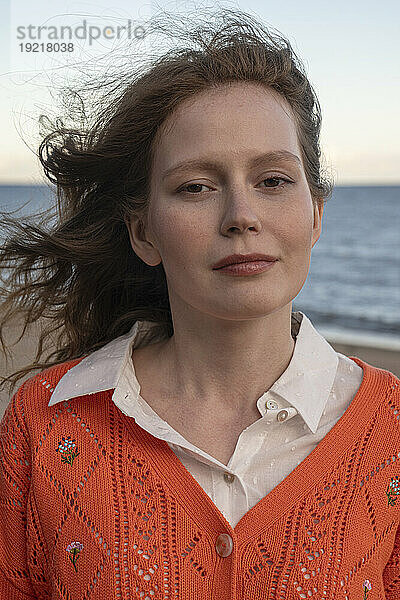 Junge Frau trägt orangefarbenen Pullover am Strand