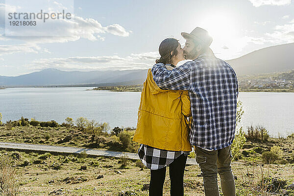 Liebevolles Paar küsst sich an einem sonnigen Tag in der Nähe des Sees