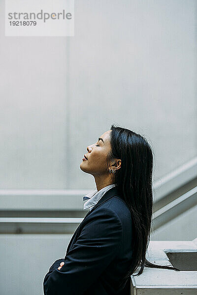 Businesswoman with eyes closed leaning on railing at workplace