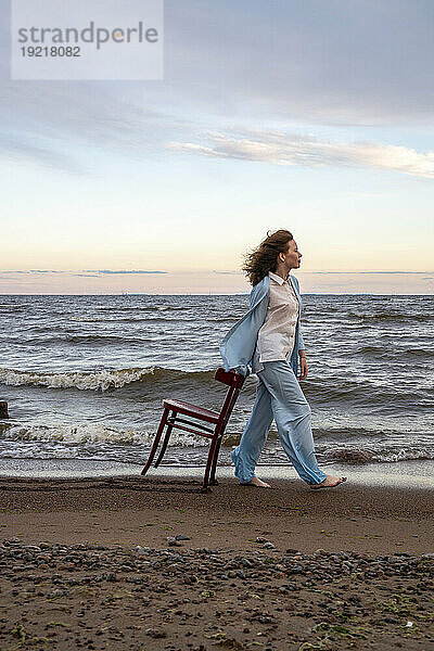 Junge Frau geht mit Stuhl am Strand spazieren
