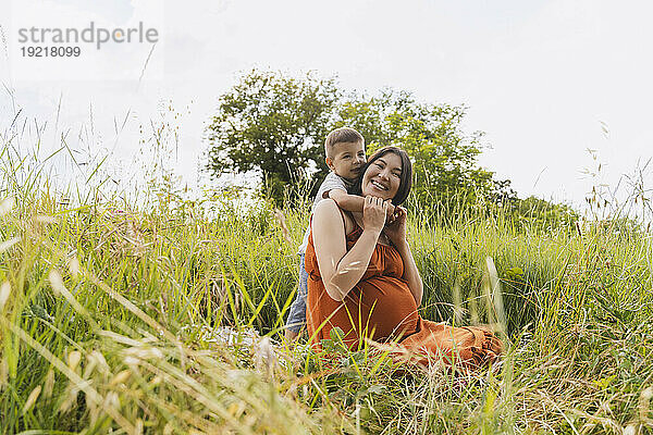 Son hugging pregnant mother in meadow