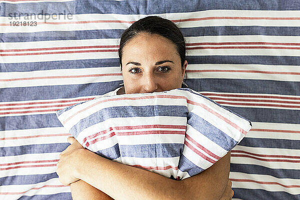Frau liegt auf dem Bett und umarmt zu Hause ein gestreiftes Kissen