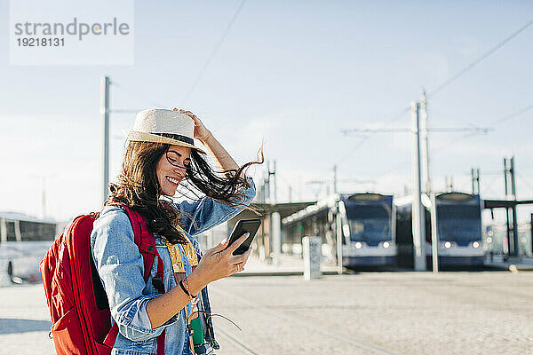 Glückliche Frau mit Hut und Smartphone an einem sonnigen Tag