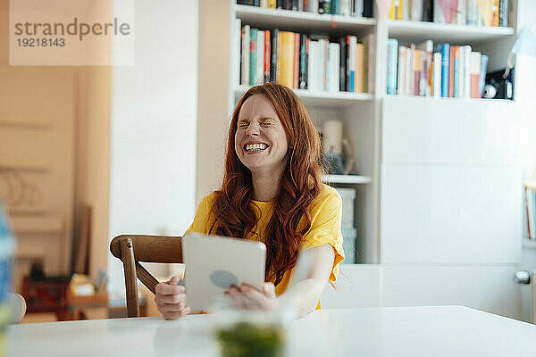 Glückliche Frau sitzt zu Hause mit Tablet-PC