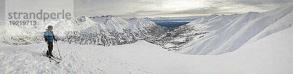 Ein Backcountry-Skifahrer nimmt sich einen Moment Zeit  um die Aussicht vom Gipfel des Hatcher Pass in Alaska zu genießen