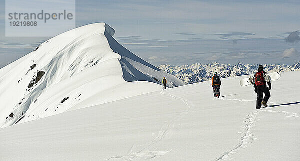 Im Hintergrund erhebt sich ein Gesims des Mt. Hawthorne  während Skifahrer und Snowboarder beim Heliskiing in der Nähe von Juneau  Alaska  wandern  um einen besseren Blick auf den Gipfel zu bekommen
