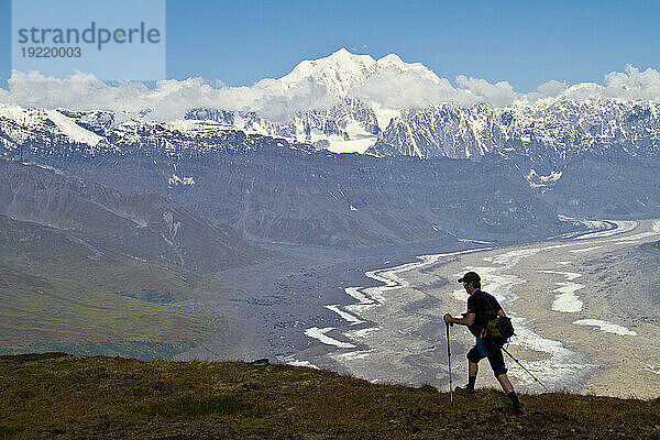 Silhouette eines Mannes  der in den Tokosha-Bergen über dem Tokositna-Gletscher wandert  mit Mt. Hunter und der Alaskakette im Hintergrund  Denali-Nationalpark und Reservat  Inneres Alaskas  Sommer