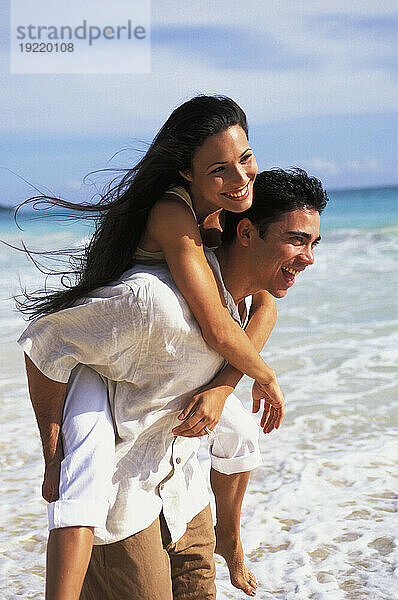 Hawaii  glückliches junges einheimisches Paar (Huckepack) in flacher Wäsche am Strand.