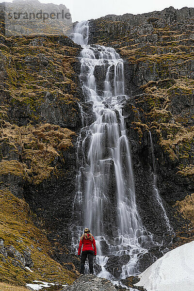 Blick von hinten auf eine Frau  die vor einem Wasserfall an der Strandir-Küste in der Nähe der Stadt Djupavik im Nordwesten Islands steht; Djupavik  Westfjorde  Island