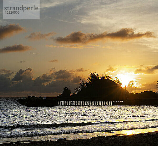 Silhouette eines Kais am Strand in der Dämmerung mit goldenem Licht  das sich am Ufer spiegelt  entlang der Straße nach Hana  malerische Route; Maui  Hawaii  Vereinigte Staaten von Amerika