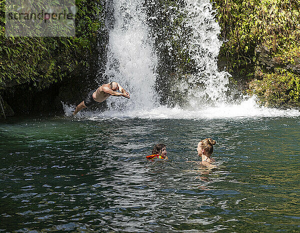 Familie genießt das Schwimmen in einem natürlichen Pool unter einem stürzenden Wasserfall entlang der Straße nach Hana; Maui  Hawaii  Vereinigte Staaten von Amerika