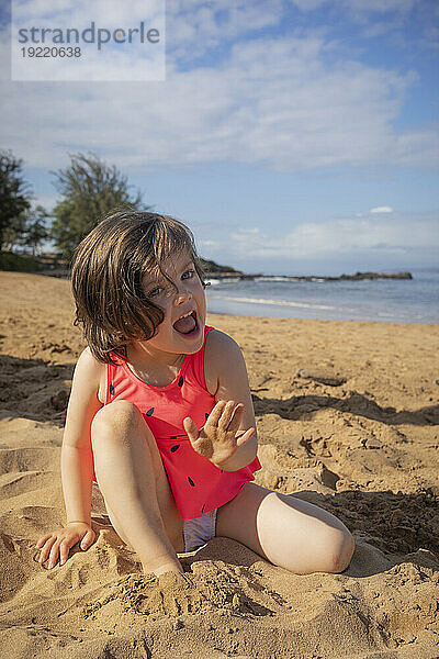 Junges Mädchen blickt mit aufgeregtem Gesichtsausdruck in die Kamera  zeigt ihre sandige Hand und genießt Kamaole Beach; Maui  Hawaii  Vereinigte Staaten von Amerika