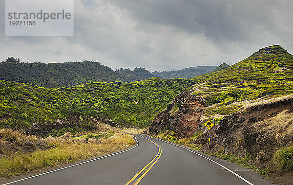 Kurvenreiche Straße mit Verkehrszeichen und bewölktem Himmel durch die grünen Hügel entlang einer malerischen Fahrt in West Maui; Maui  Hawaii  Vereinigte Staaten von Amerika