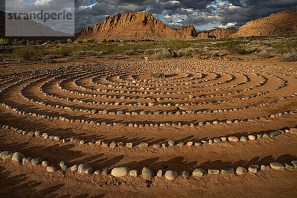 Wanderweg durch den Snow Canyon  mit Steinkreisen in einem Treffpunkt hinter dem Red Mountain Spa  mit Meditationslabyrinth und der Snow Canyon Mountain Range im Hintergrund. Red Cliffs Desert Reserve rund um St. George Town mit Felsklippen und dunklen Wolken am blauen Himmel; St. George  Utah  Vereinigte Staaten von Amerika