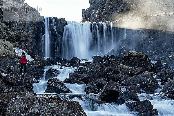 Frau steht in der Nähe eines Wasserfalls etwas außerhalb von Seyðisfjörður in den Ostfjorden Islands; Ostisland  Island