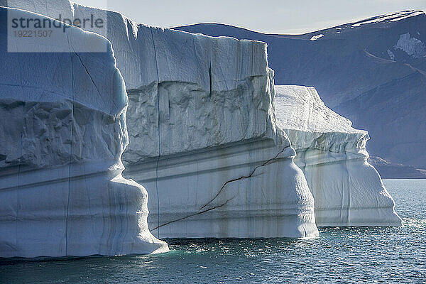 Nahaufnahme eines großen Eisbergs mit schlammigen Streifen  der im eisblauen Wasser des Kaiser-Franz-Joseph-Fjords in Grönland schwimmt; Ostgrönland  Grönland