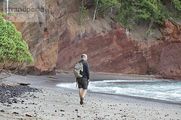 Blick von hinten auf einen Mann  der zwischen den felsigen Meeresklippen am Strand entlang geht und auf den Pazifischen Ozean auf der Straße nach Hana blickt; Maui  Hawaii  Vereinigte Staaten von Amerika