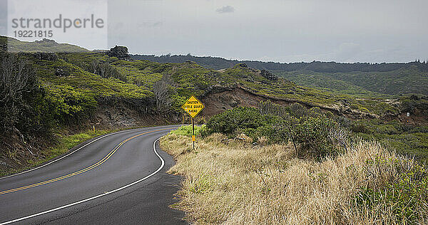 Blick auf eine kurvenreiche Straße mit Verkehrszeichen durch die grünen Hügel auf einer malerischen Fahrt an einem bewölkten Tag in West Maui; Maui  Hawaii  Vereinigte Staaten von Amerika