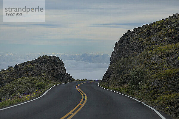 Gepflasterte Autobahn mit Blick auf die Wolken durch die felsigen Klippen des Berghangs auf der Straße hinunter von Haleakala; Maui  Hawaii  Vereinigte Staaten von Amerika