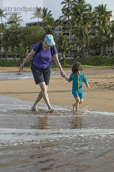 Großmutter und Enkelin gehen Hand in Hand die Brandung am Kamaole Beach vor einem Resort entlang; Maui  Hawaii  Vereinigte Staaten von Amerika